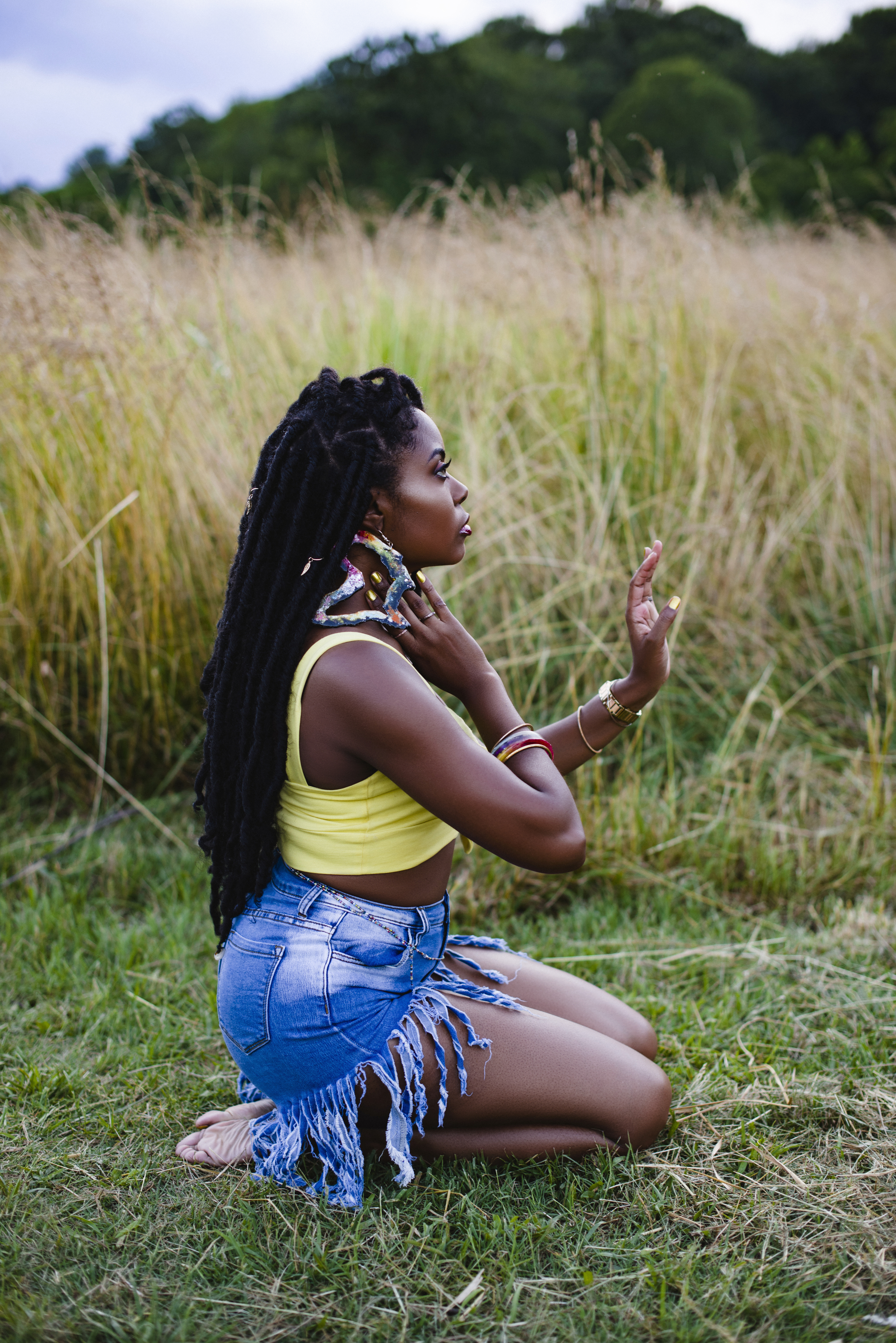 Kneeling in tall golden grass, adjusting an earring, side profile