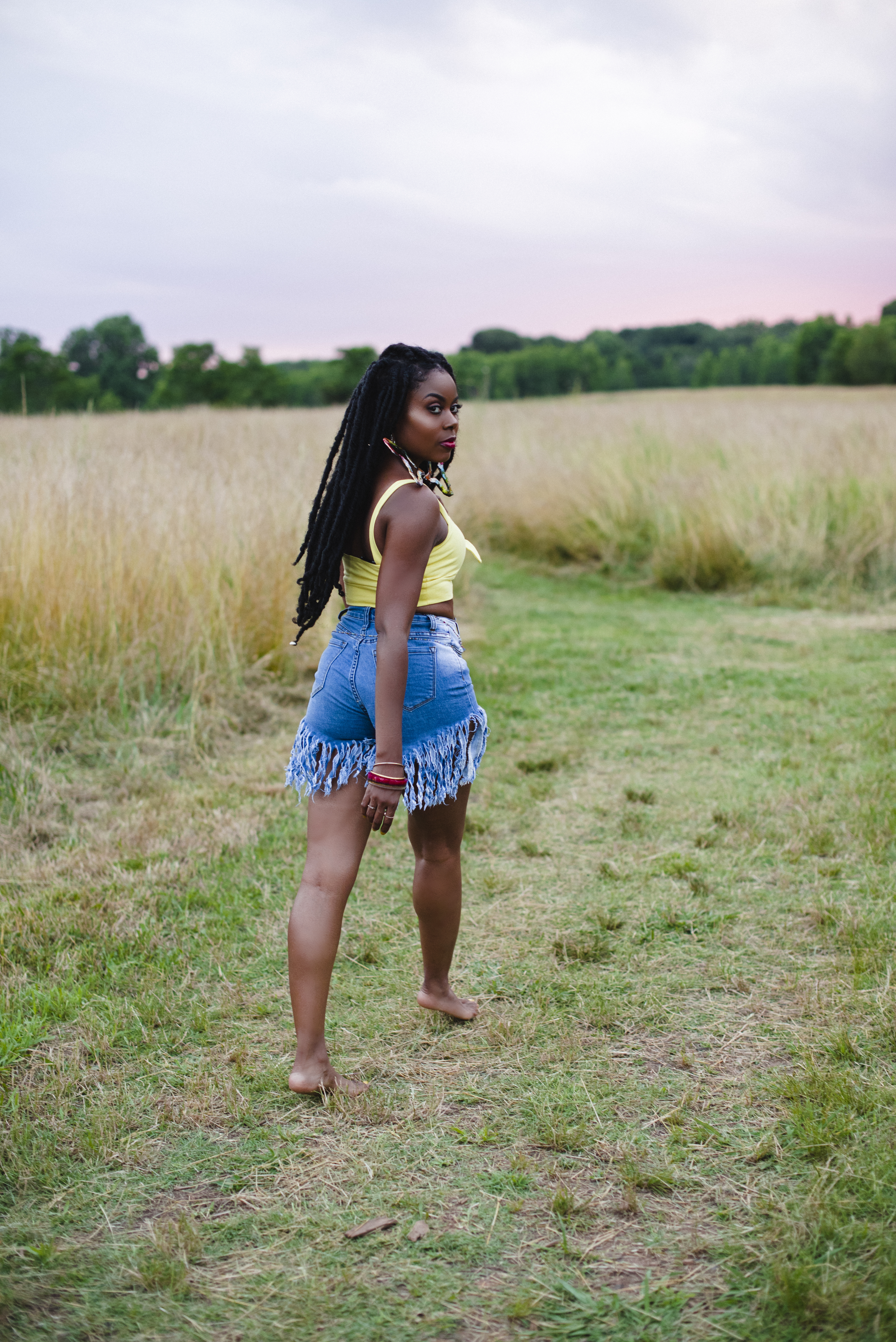 Walking away down a grassy path into the field at dusk, looking back over her shoulder