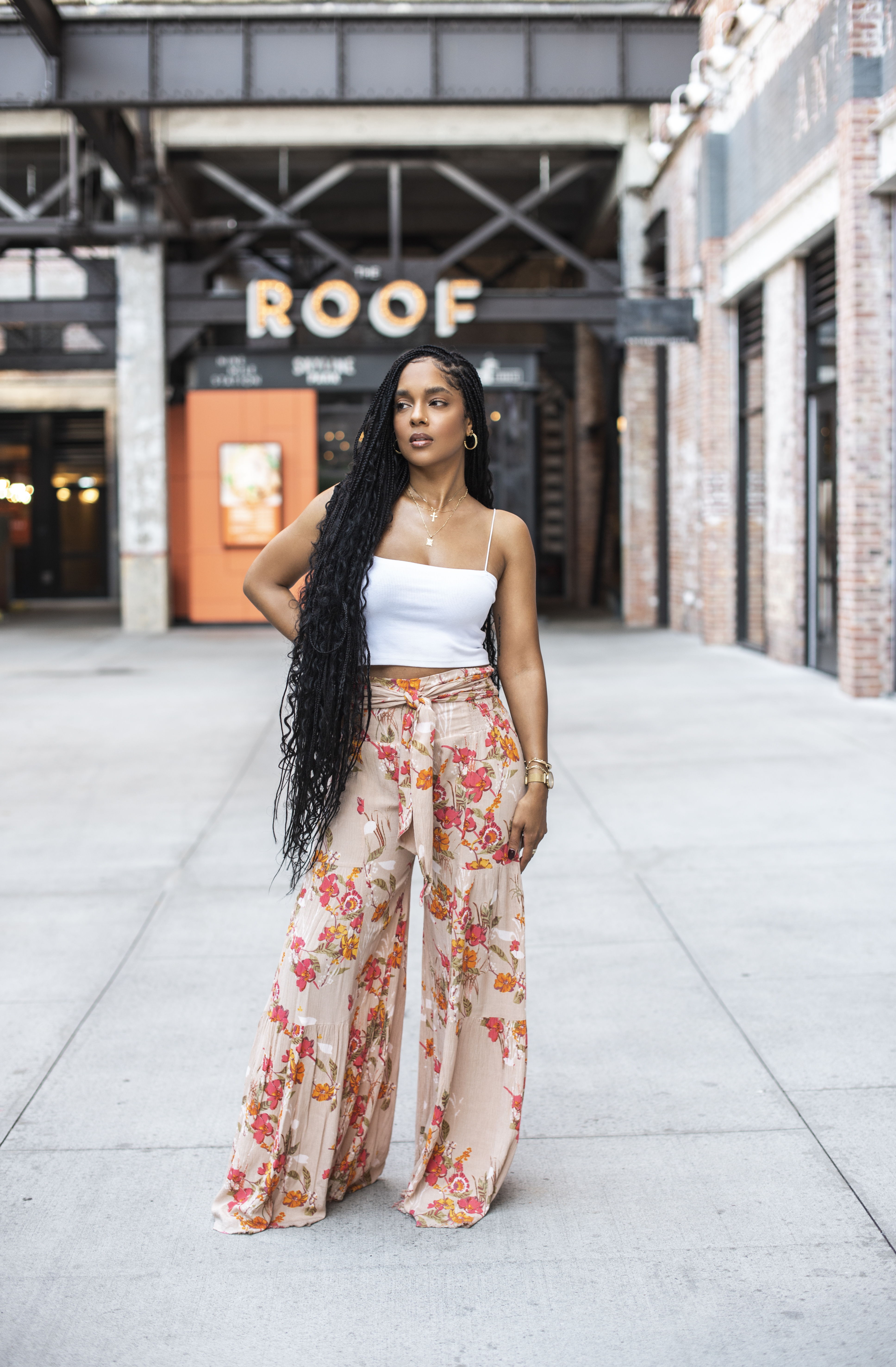 Standing in a downtown Atlanta courtyard in flowy floral pants and a white tank top, long braids down her back