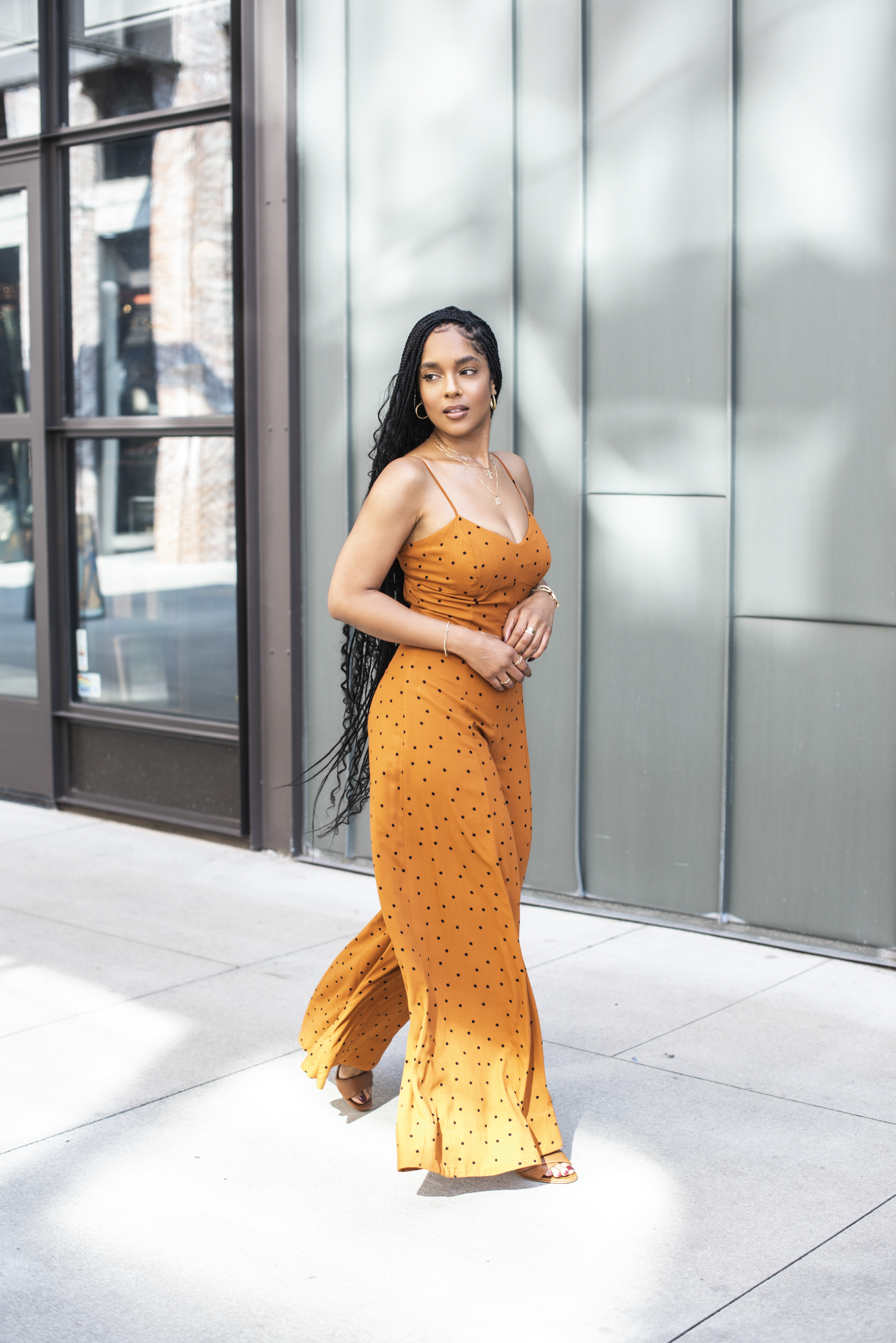 Walking through a sunlit downtown plaza in an orange polka-dot jumpsuit