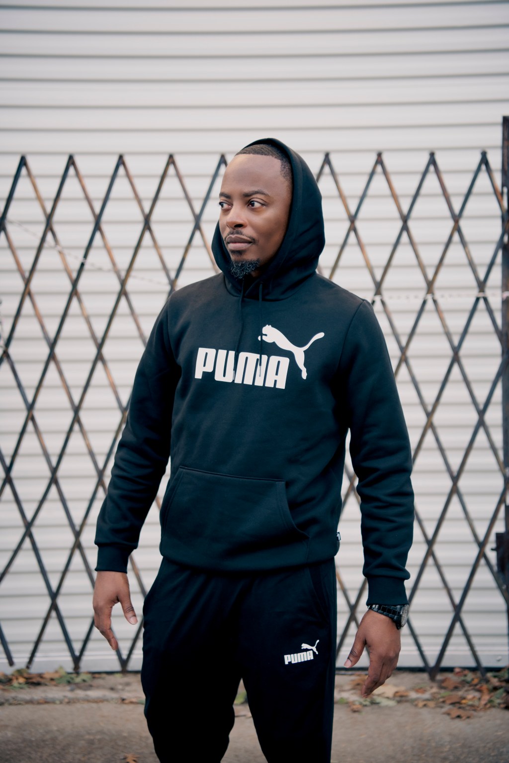 Front-facing portrait in a black Puma hoodie in front of a lattice metal gate