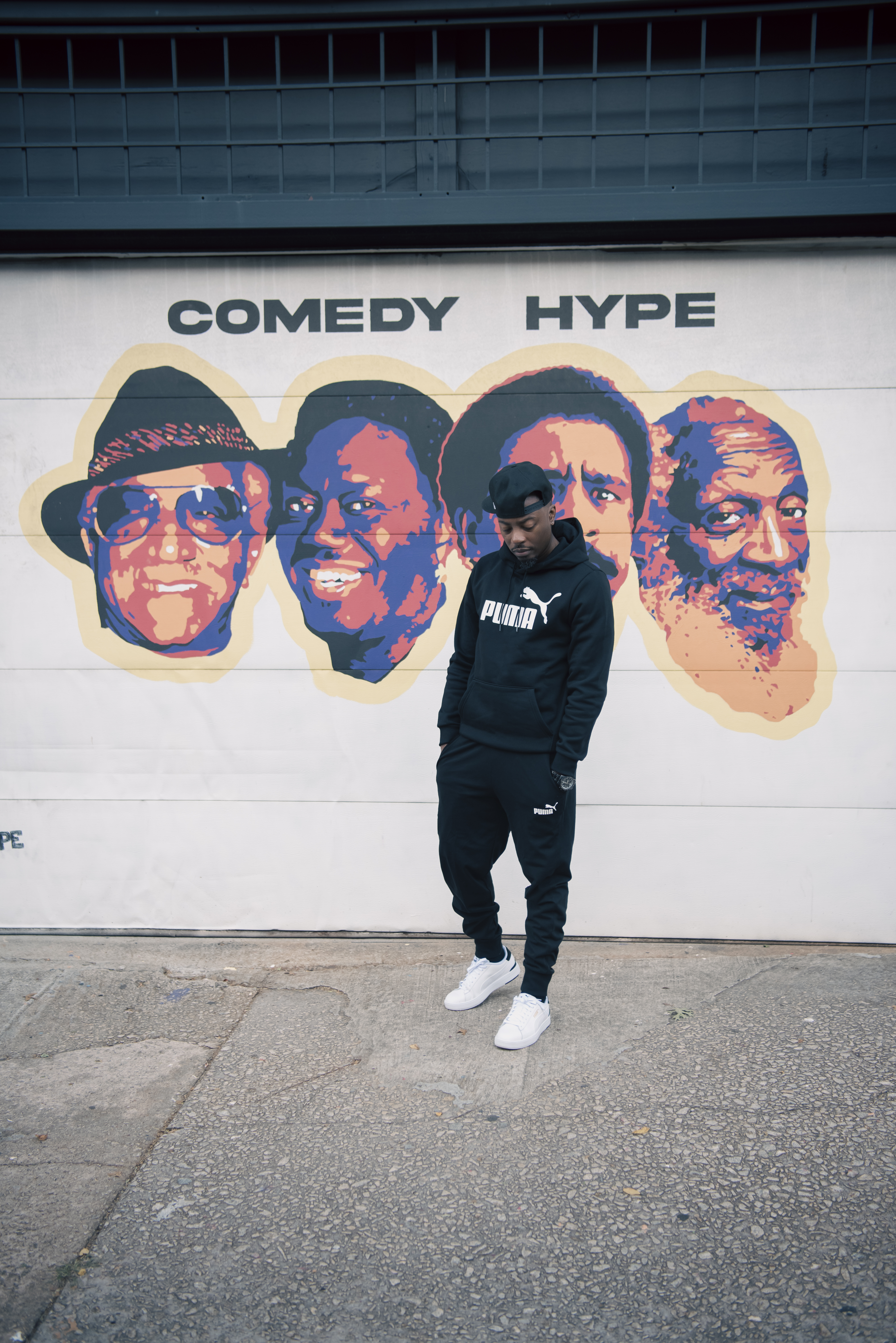 Standing in a black Puma sweatsuit in front of a Comedy Hype mural